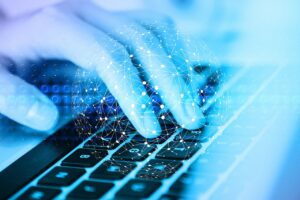 A close-up of a hand typing on a keyboard with a glowing blockchain network in the background, symbolising digital technology and cryptocurrency.