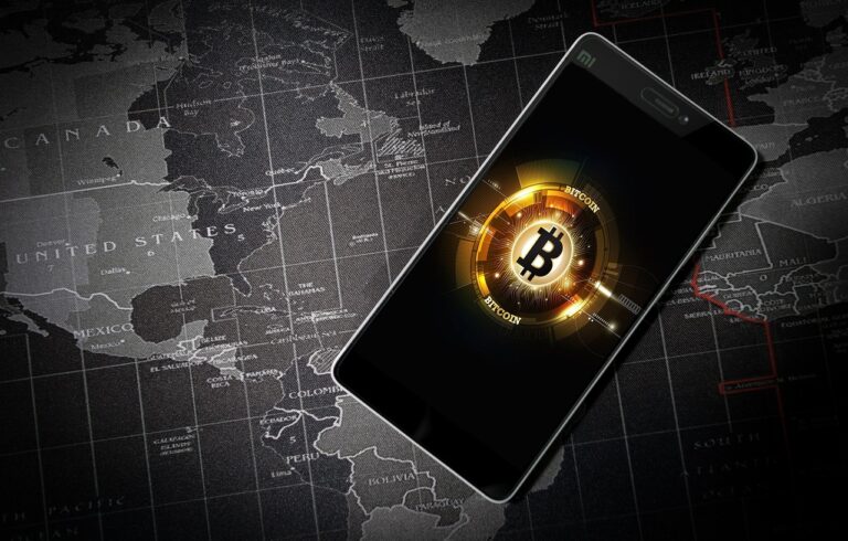 A golden Bitcoin coin standing upright on a reflective surface, with financial charts and market data displayed in the blurred background, symbolising cryptocurrency trading and market trends.