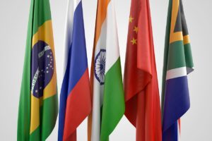 Flags of China, Brazil, and Russia waving against a clear blue sky, representing BRICS nations.