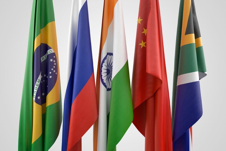 Flags of China, Brazil, and Russia waving against a clear blue sky, representing BRICS nations.